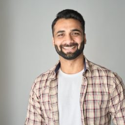 Headshot portrait of attractive confident indian Hispanic man with toothy smile looking at camera at modern living room. Latin businessman posing in casual stylish look at home office.