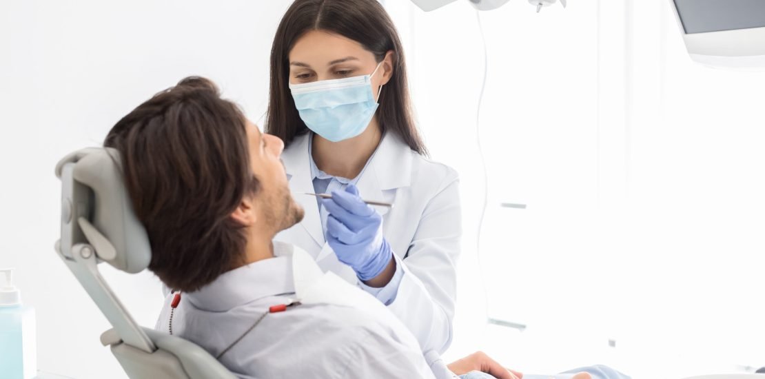 Side view of man having check up in new dental office, assisting by young professional dentist, copy space