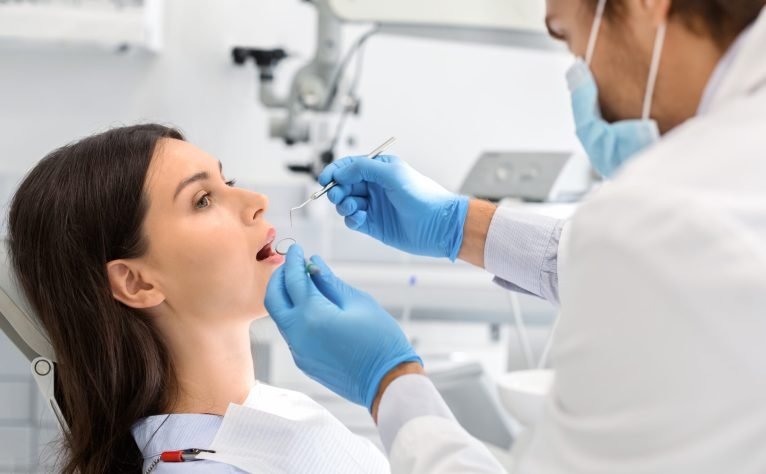 Young woman having regular check up in newest dental office, male dentist in gloves and mask holding dental tools, free space